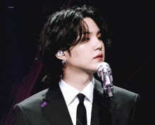 a man in a suit and tie is singing into a microphone with a purple ribbon around his neck