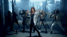a woman in a silver coat is dancing with a group of dancers