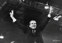 a man in a suit and tie is raising his arms in the air in front of a crowd