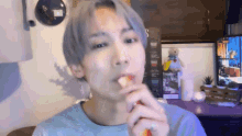 a young man with gray hair is eating a strawberry in front of a television .