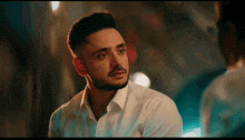 a man with a beard is wearing a white shirt and looking at another man