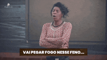 a woman stands with her arms crossed in front of a sign that says vai pegar fogo nesse feno