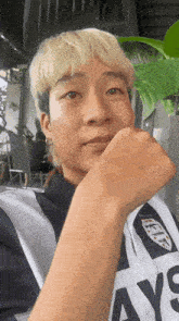 a young man with blonde hair is wearing a striped shirt and holding his fist to his chin .