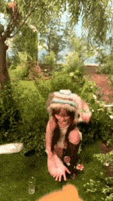 a girl in a furry hat is kneeling down in a garden