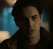 a close up of a man 's face with curly hair wearing a red jacket .