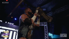 a wrestler is holding a championship belt in front of a sign that says gell