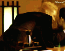 a blurry picture of a person sitting at a table with a lamp in the background and the name alismithc on the bottom right