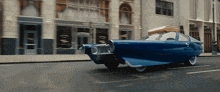a blue car is driving down a street in front of a store