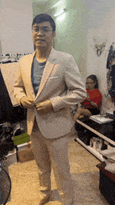 a man in a tan suit adjusts his jacket while a girl sits on a shelf