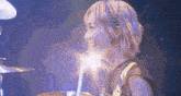 a woman is playing drums on a stage with a purple background