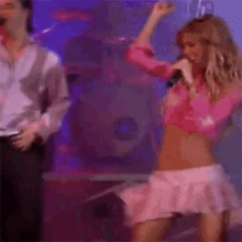 a woman in a pink top and pink skirt is singing into a microphone on stage