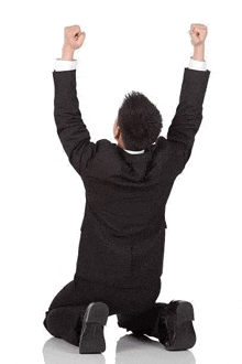 a man in a suit is kneeling on the floor with his arms in the air .
