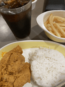 a plate of fried chicken rice and french fries next to a cup of soda