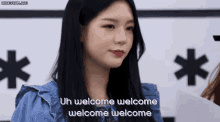 a woman with long black hair is standing in front of a sign that says uh welcome welcome welcome welcome