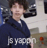 a young man in a blue jacket is standing in a parking garage with the words js yappin written on the bottom .