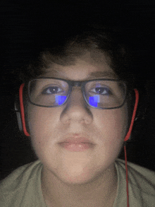 a young boy wearing glasses and headphones looks at the camera in the dark