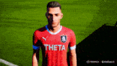 a man in a red theta jersey stands on a field