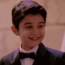 a young boy wearing a tuxedo and bow tie smiles for the camera