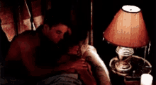 a man and woman are kissing in a bed next to a lamp