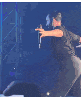 a man in a black shirt is singing into a microphone on stage .