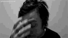 a man is covering his face with his hands while smoking a cigarette .