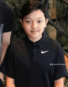 a young boy wearing a black nike shirt stands in front of a skeleton