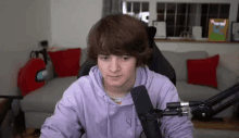 a young man wearing a purple hoodie is sitting in front of a microphone in a living room .