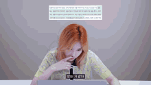 a woman with red hair is sitting in front of a laptop with a foreign language displayed on the screen