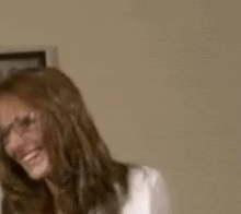 a woman in a white shirt is smiling and looking at the camera in a room .
