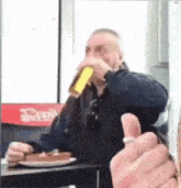 a man is drinking a beer while sitting at a table in front of a coca cola machine .
