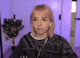 a woman wearing headphones and a sweater looks at the camera with a plant in the background