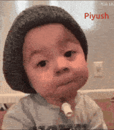 a baby wearing a knitted hat with the name piyush on the bottom right