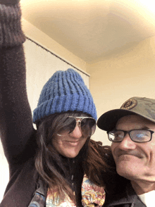 a woman wearing a blue hat and sunglasses stands next to a man wearing glasses and a hat that says boston