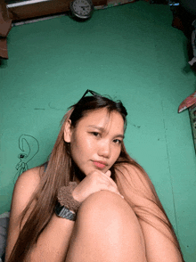 a woman sitting in front of a green wall with a clock on it that shows the time as 10:08