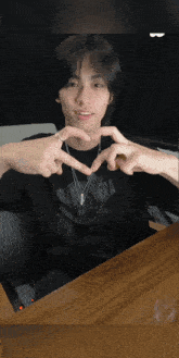 a young man making a heart shape with his hands while wearing a black shirt with the word era on the front