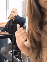 a woman is sitting at a table smoking a cigarette while a man drinks from a glass .