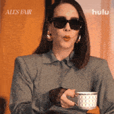 a woman wearing sunglasses is blowing a kiss while holding a cup of coffee in front of a sign that says hulu