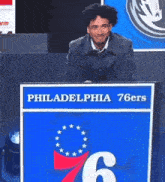 a man sits behind a podium that says philadelphia 76ers