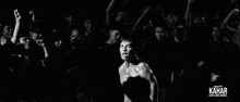 a man without a shirt is standing in front of a crowd of people with their hands in the air .
