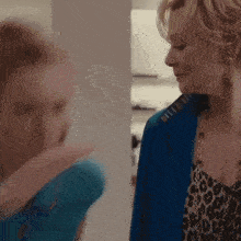 a woman wearing a blue jacket and a leopard print top is talking to another woman