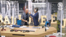 two men are shaking hands in front of a sign that says rai