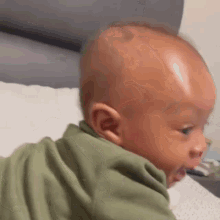 a baby in a green shirt is crawling on a bed and looking at the camera .