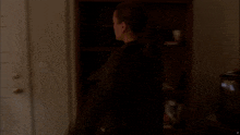 a woman opens a door in a dark room next to a bookshelf with books on it
