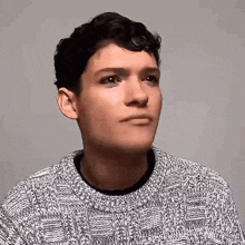 a young man is wearing a sweater and making a funny face .