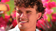 a man with curly hair is smiling with a pink background