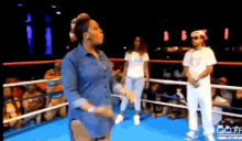 a woman is dancing in a boxing ring while a man stands behind her