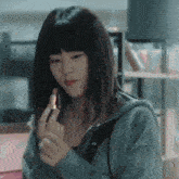 a woman in a blue hoodie is applying lipstick to her finger