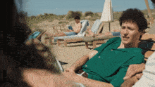 a man in a green shirt sits in a chair on a beach