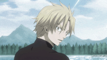 a man with blonde hair and a black shirt stands in front of a body of water