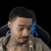 a man with a tattoo on his chest is sitting in a chair with a black background .